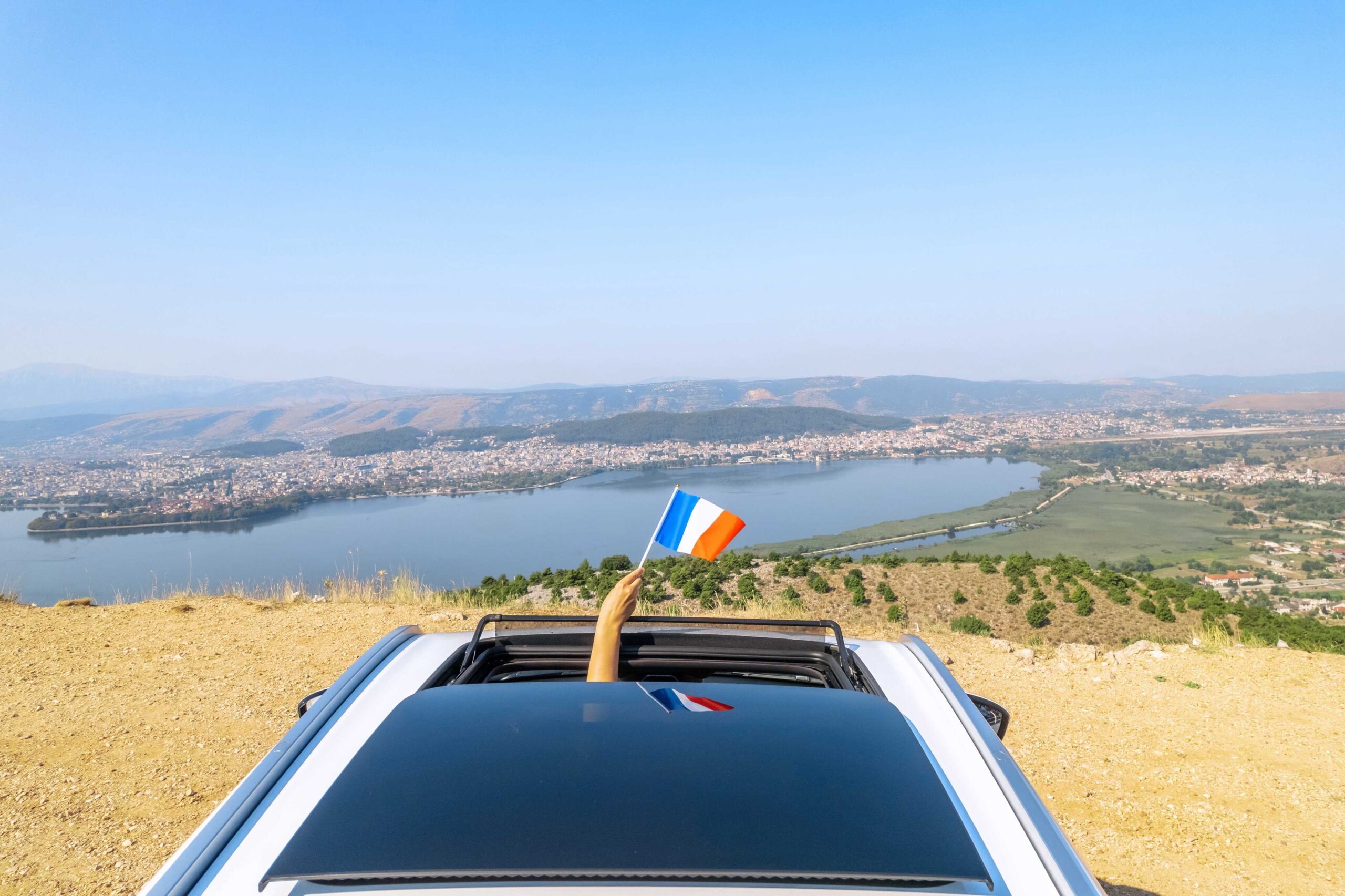 Person waving a French flag from a car window demonstrating why people hiring a car abroad should get car rental excess insurance.