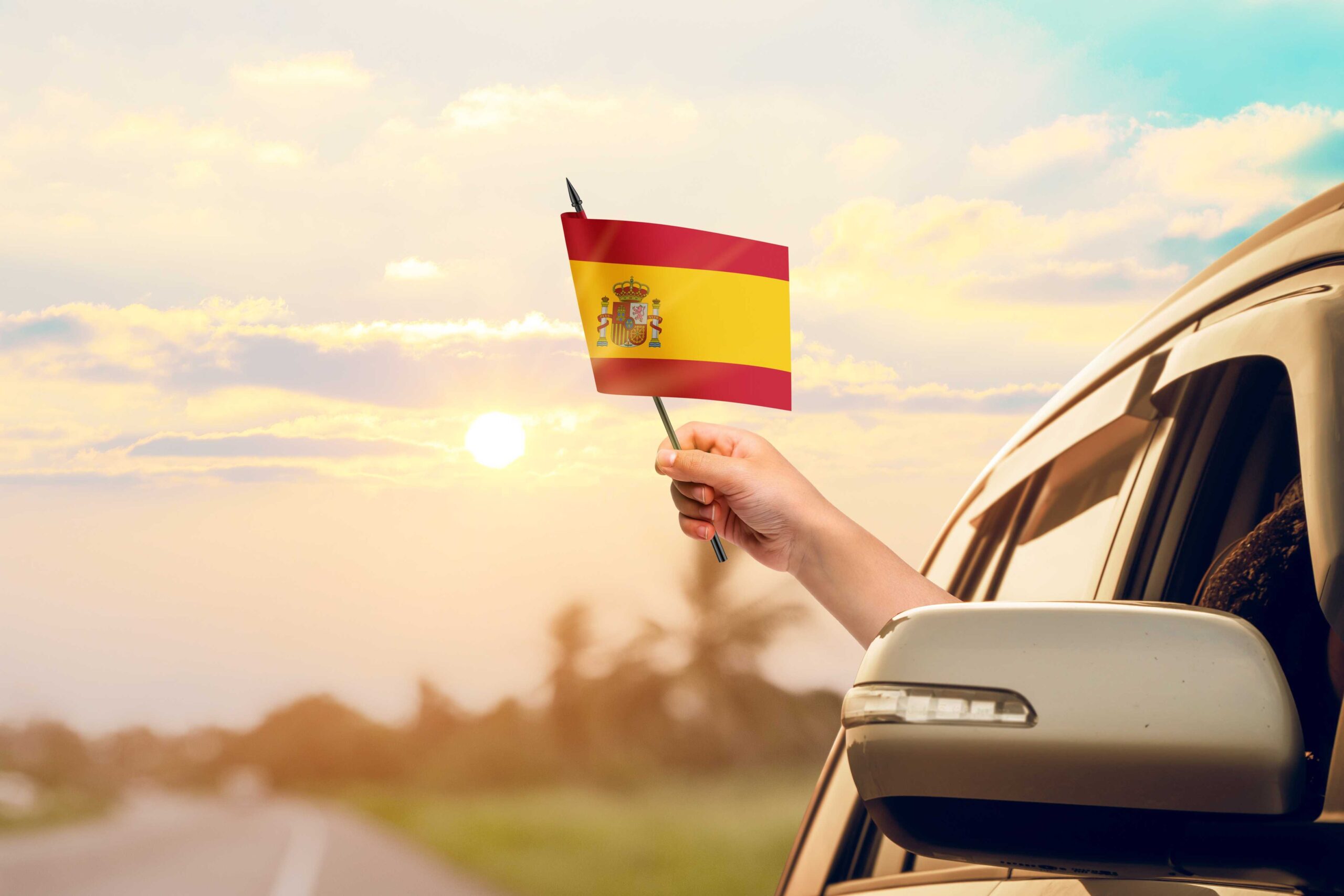 Person waving a Spanish flag from a car window, highlighting the importance of car rental excess insurance for people hiring cars.