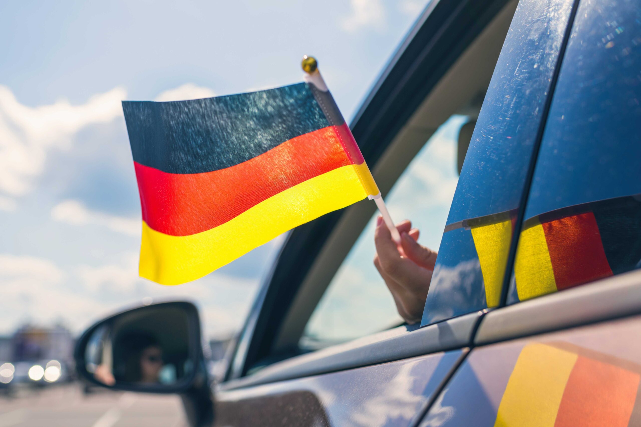 Person holding German flag outside of car window reinforcing importance of car rental excess insurance for people renting cars.